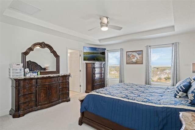 bedroom with light carpet, a tray ceiling, visible vents, and a ceiling fan