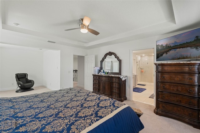 carpeted bedroom featuring ensuite bathroom, a ceiling fan, visible vents, baseboards, and a tray ceiling