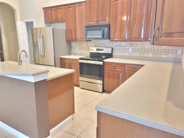 kitchen featuring light tile patterned floors, brown cabinets, stainless steel appliances, light countertops, and backsplash