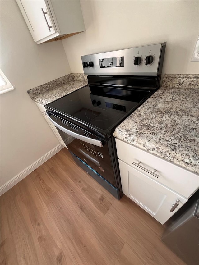 kitchen featuring electric stove, white cabinets, light wood-style flooring, and baseboards