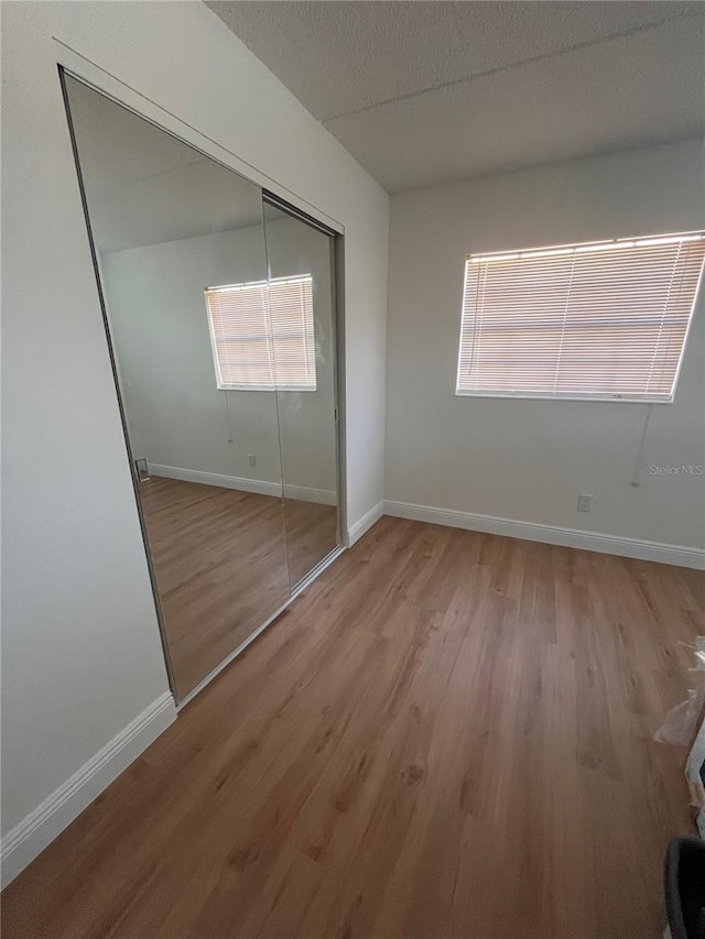 unfurnished bedroom with a closet, a textured ceiling, baseboards, and wood finished floors