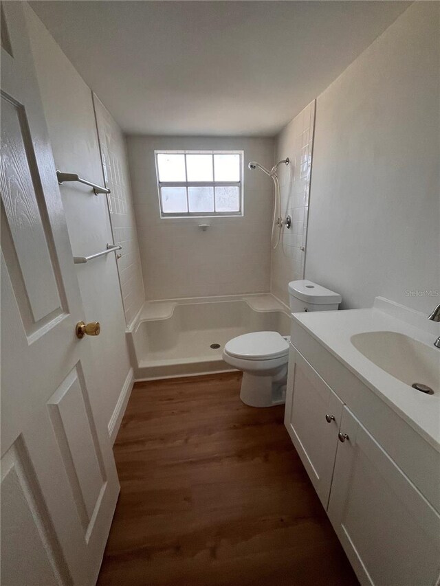 bathroom featuring toilet, walk in shower, wood finished floors, and vanity