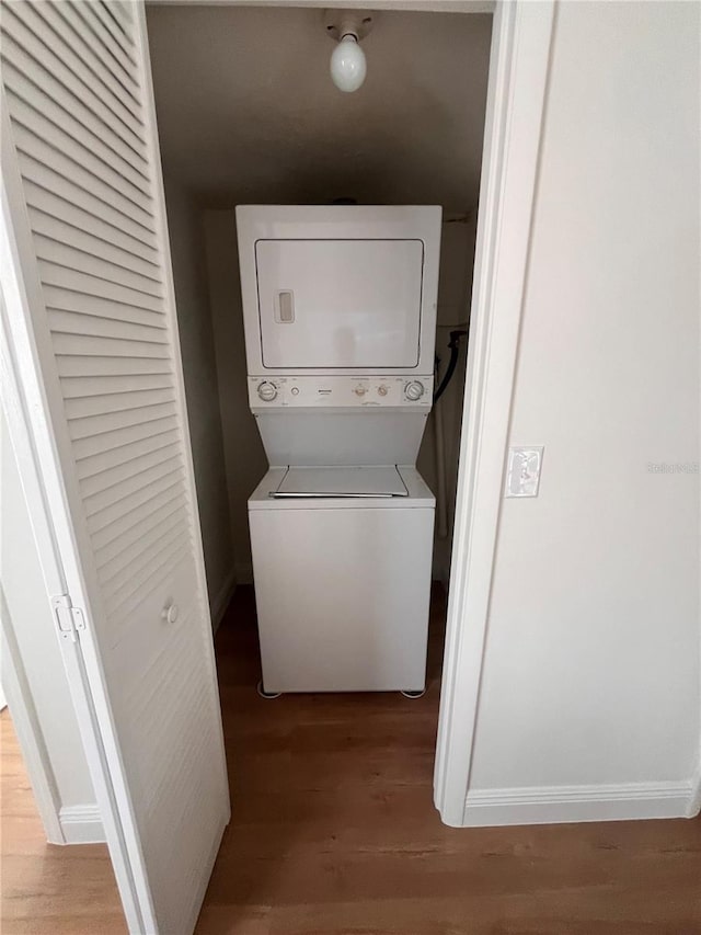 laundry room featuring stacked washer / dryer, laundry area, baseboards, and wood finished floors