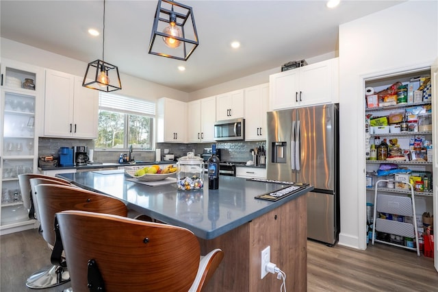 kitchen featuring stainless steel appliances, dark countertops, a kitchen breakfast bar, and wood finished floors