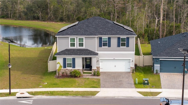 view of front of property with a water view, roof mounted solar panels, fence, stone siding, and a front lawn