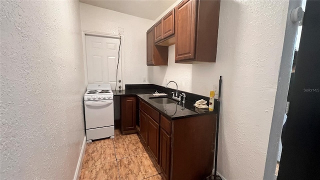 kitchen with a sink, dark countertops, electric stove, and a textured wall