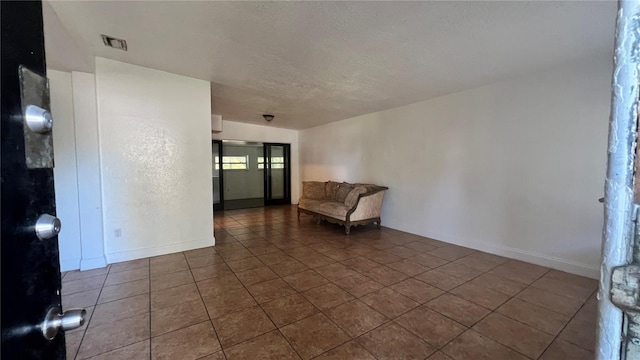 unfurnished room featuring dark tile patterned flooring, visible vents, a textured ceiling, and baseboards