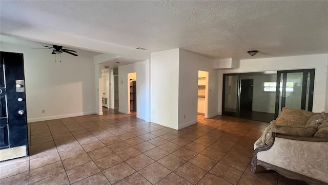 unfurnished living room featuring baseboards, a ceiling fan, a textured ceiling, and tile patterned floors