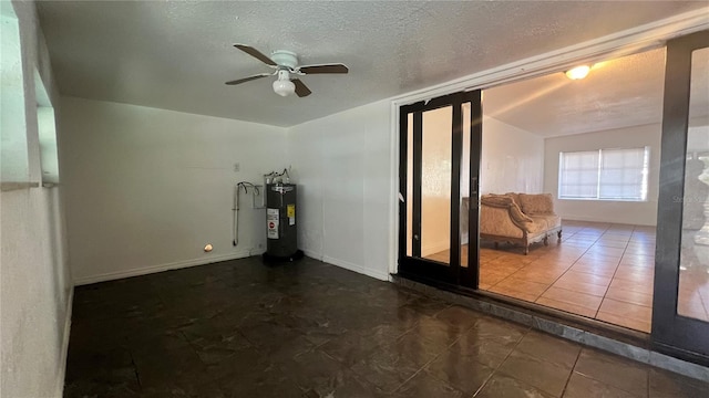 unfurnished room with a ceiling fan, electric water heater, a textured ceiling, dark tile patterned flooring, and baseboards