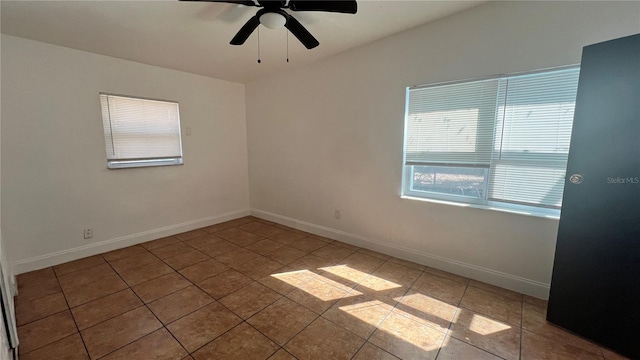 tiled empty room featuring ceiling fan and baseboards