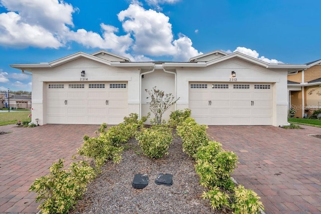 single story home featuring decorative driveway, an attached garage, and stucco siding