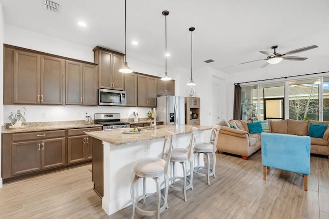 2312 Datura Loop, Saint Cloud, FL 34772 - kitchen with light stone counters, stainless steel appliances, visible vents, light wood-style floors, and open floor plan