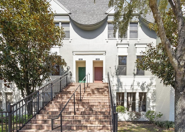 view of front of property featuring a shingled roof, stairway, and stucco siding