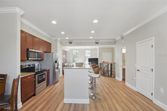 kitchen with a kitchen breakfast bar, open floor plan, ornamental molding, appliances with stainless steel finishes, and light wood-type flooring