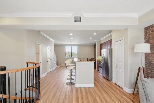 kitchen with light wood-style flooring, a breakfast bar, stainless steel appliances, crown molding, and light countertops