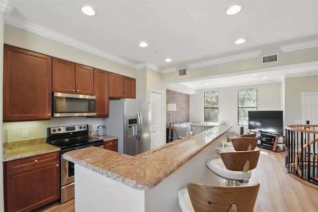 kitchen featuring a breakfast bar area, visible vents, appliances with stainless steel finishes, light wood-style floors, and open floor plan