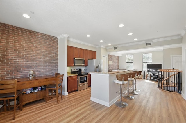 kitchen with brick wall, visible vents, appliances with stainless steel finishes, light wood finished floors, and a kitchen bar