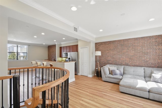 living room featuring brick wall, visible vents, baseboards, light wood-style floors, and crown molding