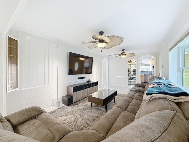 living area featuring ornamental molding, arched walkways, and ceiling fan