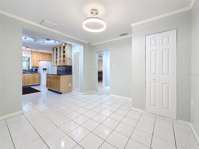 kitchen featuring white refrigerator with ice dispenser, crown molding, light tile patterned floors, dark countertops, and visible vents