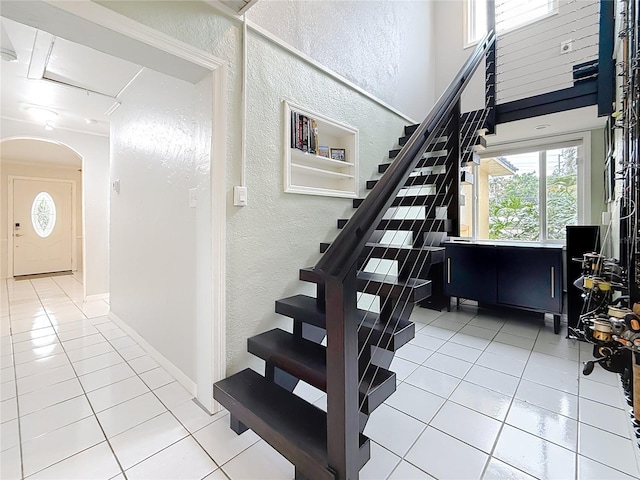 stairway with arched walkways, a textured wall, a high ceiling, tile patterned flooring, and baseboards