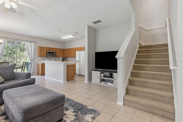 living area featuring light tile patterned floors, visible vents, stairway, a ceiling fan, and a textured ceiling