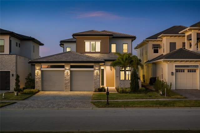 prairie-style home with stone siding, an attached garage, and decorative driveway