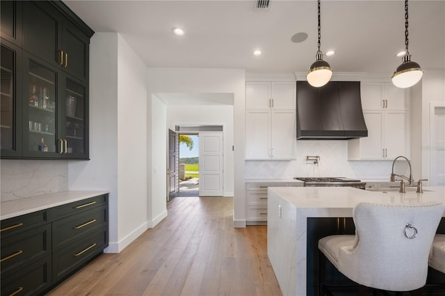 kitchen with glass insert cabinets, tasteful backsplash, light wood-style floors, and custom range hood