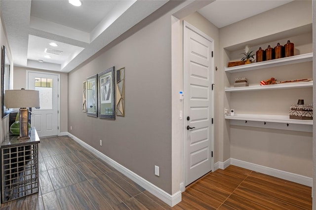 foyer entrance with dark wood-type flooring, a tray ceiling, visible vents, and baseboards