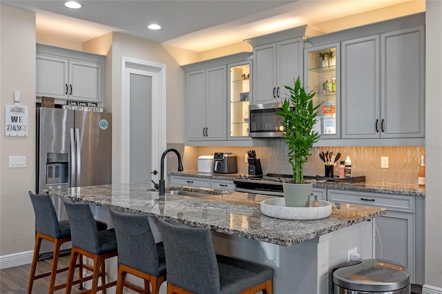 kitchen with stainless steel appliances, a breakfast bar area, backsplash, and gray cabinetry