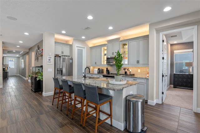 kitchen with a breakfast bar area, a sink, appliances with stainless steel finishes, tasteful backsplash, and a center island with sink