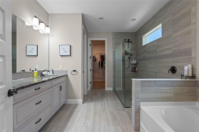 bathroom featuring a bath, a walk in closet, tiled shower, and vanity