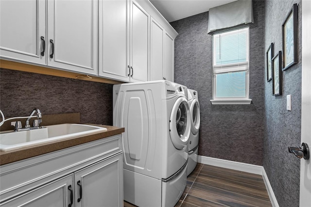 clothes washing area featuring a sink, washing machine and dryer, cabinet space, and wallpapered walls