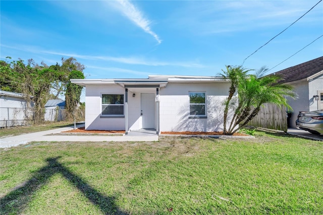 view of front facade featuring a front yard, concrete block siding, and fence