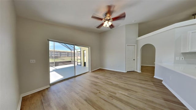 spare room featuring arched walkways, baseboards, a ceiling fan, light wood-style flooring, and vaulted ceiling