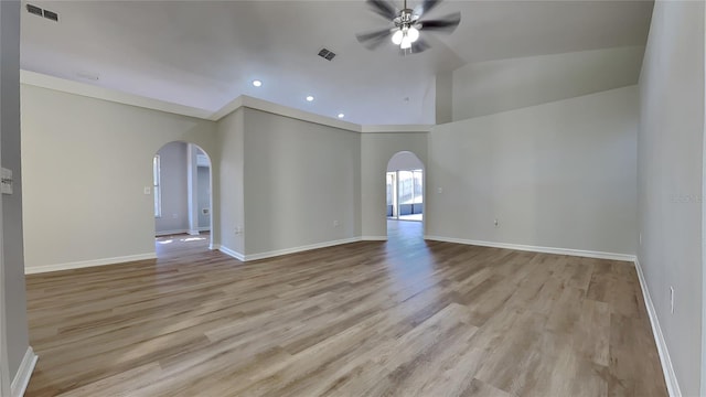 spare room featuring visible vents, arched walkways, a ceiling fan, vaulted ceiling, and light wood-type flooring