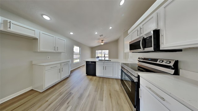 kitchen featuring stainless steel appliances, a peninsula, a sink, white cabinetry, and light wood-style floors