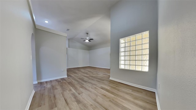 spare room featuring arched walkways, wood finished floors, a ceiling fan, and baseboards