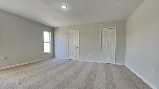 unfurnished bedroom with light carpet, multiple closets, and baseboards