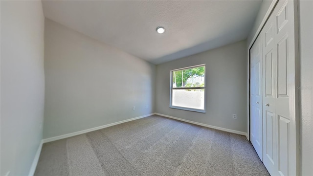 unfurnished bedroom with lofted ceiling, a closet, carpet flooring, and baseboards