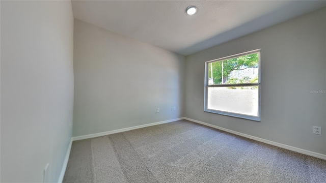 spare room featuring vaulted ceiling, carpet flooring, and baseboards