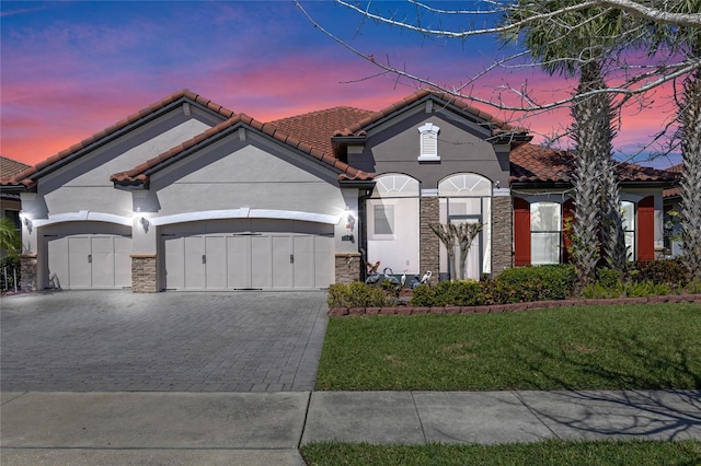 mediterranean / spanish-style house with a garage, stone siding, decorative driveway, and a tiled roof