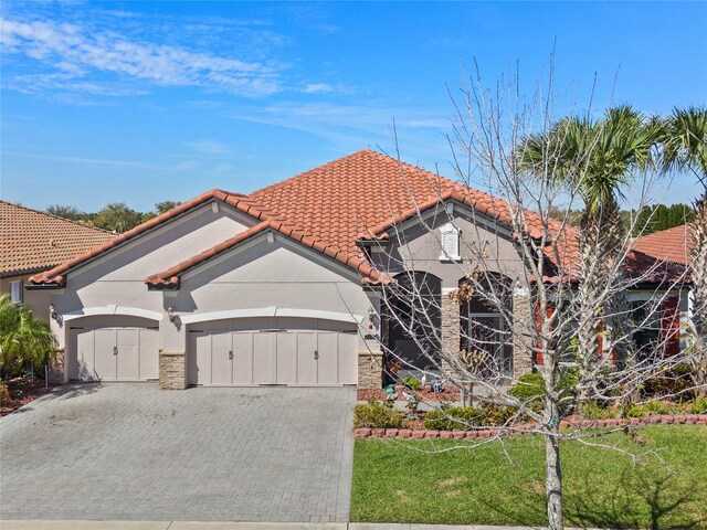2541 Shoal Bass Way, Kissimmee, FL 34746 - mediterranean / spanish-style home featuring a garage, a tile roof, decorative driveway, stucco siding, and stone siding