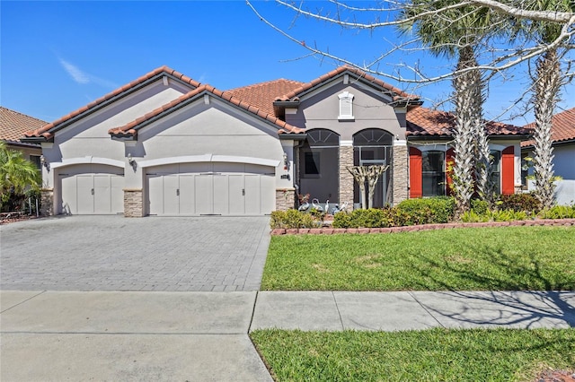 mediterranean / spanish home featuring decorative driveway, a tile roof, a garage, stone siding, and a front lawn