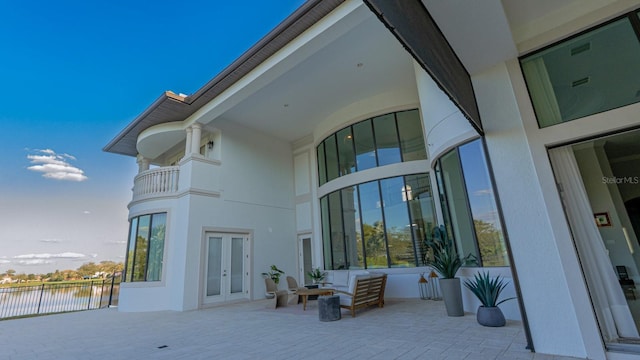 exterior space with a balcony, a water view, fence, french doors, and stucco siding