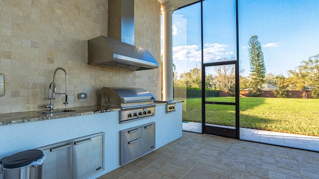 kitchen with plenty of natural light, a sink, wall chimney exhaust hood, and stone tile floors