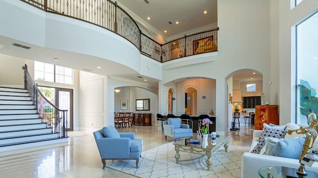 living area with arched walkways, a towering ceiling, visible vents, stairs, and ornamental molding