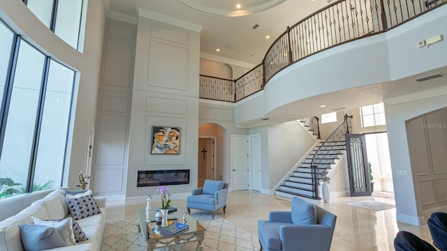 living room featuring a large fireplace, visible vents, a high ceiling, stairs, and crown molding