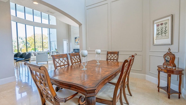 dining room featuring arched walkways, visible vents, a decorative wall, a glass covered fireplace, and baseboards