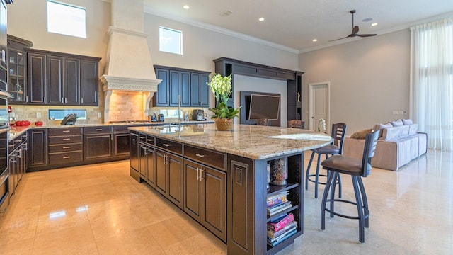 kitchen with a breakfast bar area, custom exhaust hood, open floor plan, and light stone counters